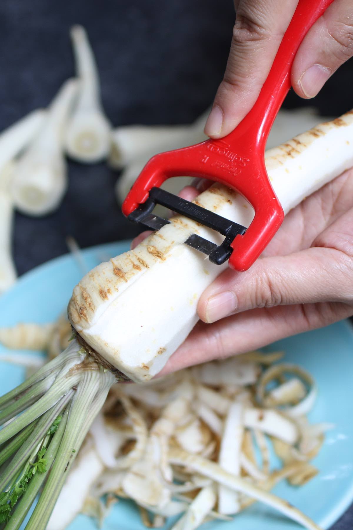 Peeling parsnips with a red peeler before roasting