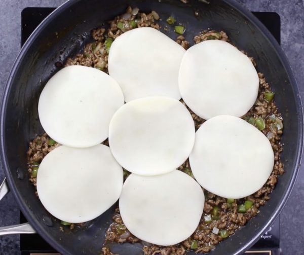 This photo shows adding the provolone cheese slices to a Philly Cheesesteak mixture in a frying pan