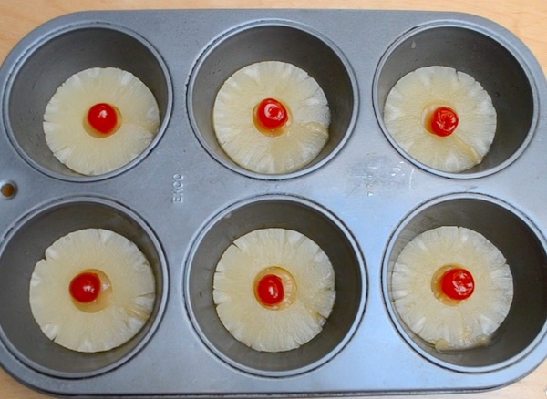 Pineapple Upside Down Cupcakes preparation showing the pineapple, brown sugar and butter mixture and cherry in a muffin tin