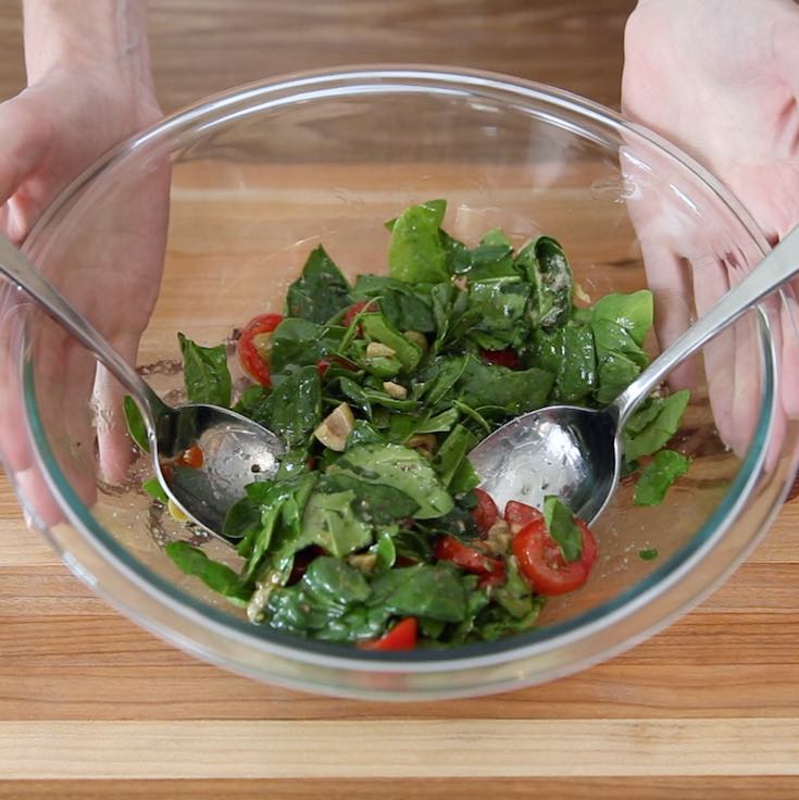 Pita Pizza toppings: spinach, tomatoes and olives being mixed together with an herbed sauce made with oregano, basil, garlic, olive oil