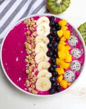 A beautiful pitaya bowl made with frozen dragon fruit, fresh bananas and almond milk with toppings including fresh mango, banana, granola and blueberries