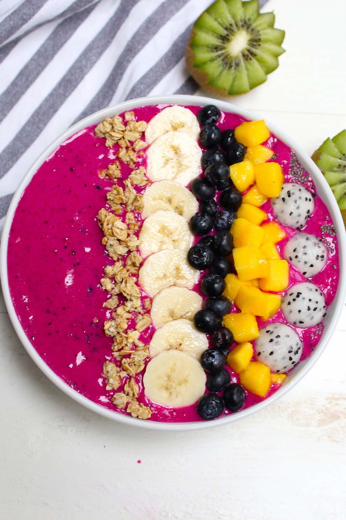 A beautiful pitaya bowl made with frozen dragon fruit, fresh bananas and almond milk with toppings including fresh mango, banana, granola and blueberries