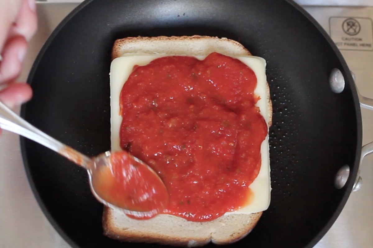 Closeup of spreading marinara sauce on top of pepperoni layer.