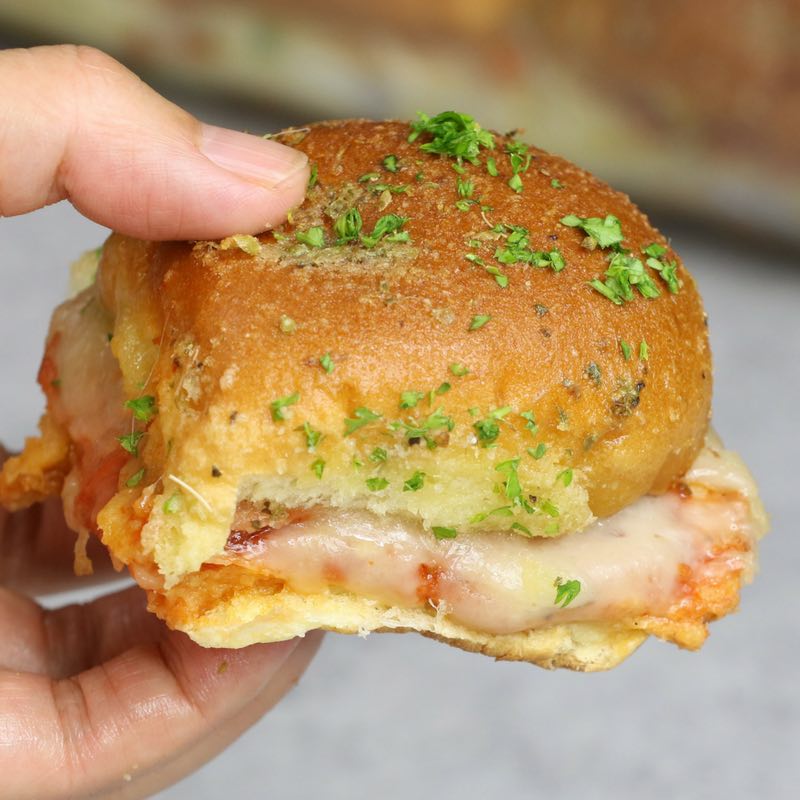 Handheld pizza slider showing melty cheese, tomato sauce and pepperoni on a dinner roll of a freshly baked pizza slider