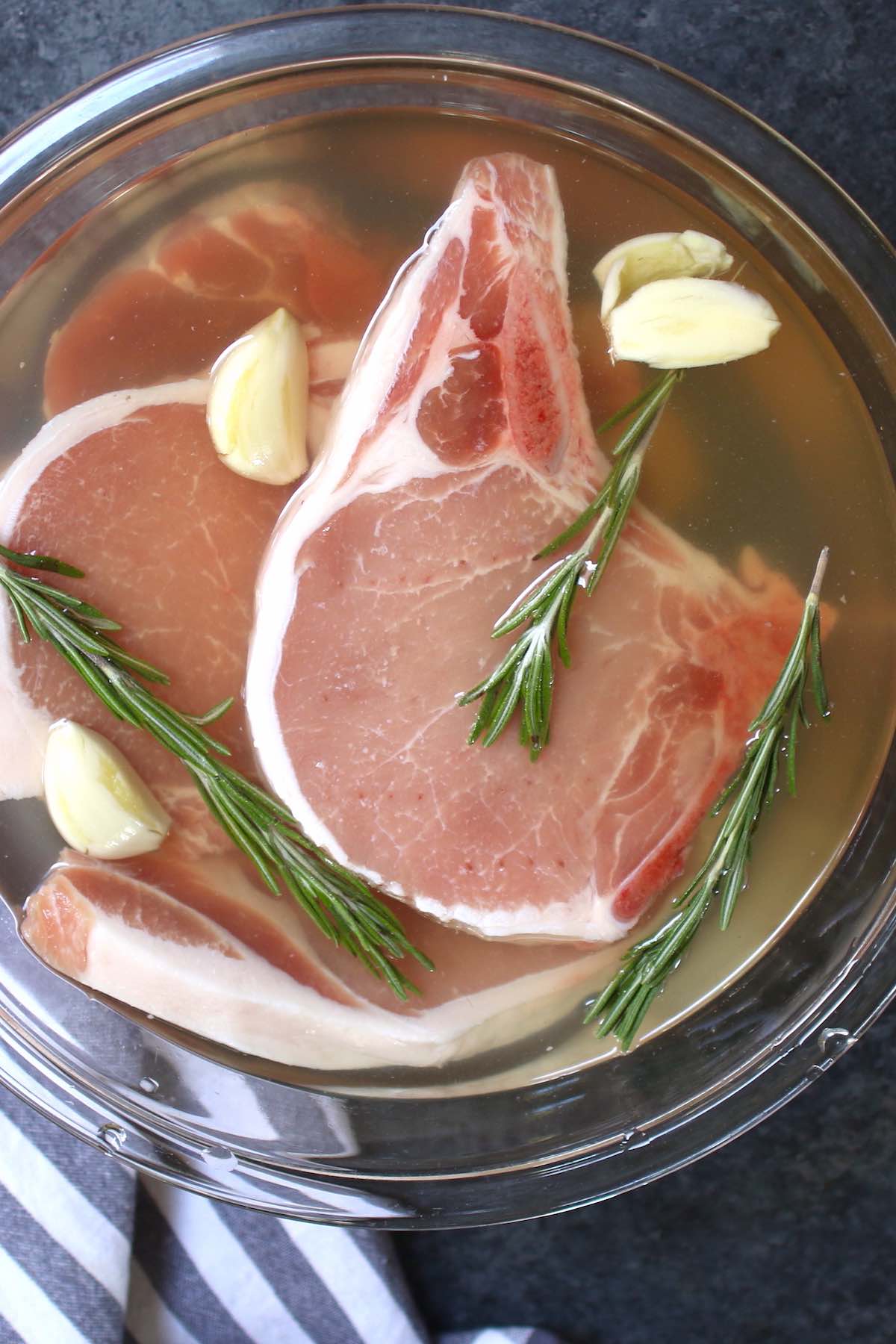 This easy pork chop brine recipe is made with salt, water, brown sugar, apple cider vinegar, rosemary, and garlic. It guarantees tender and juicy meat every time! Brined pork chops are perfect for grilling, pan-frying, or baking. #PorkChopBrine
