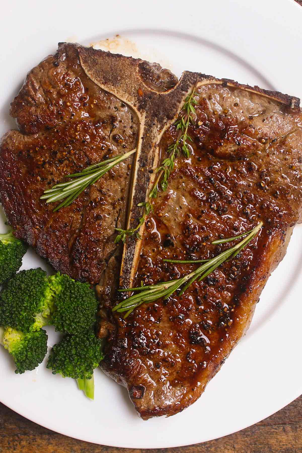 Pan seared porterhouse steak served on a serving plate garnished with sprigs of fresh rosemary and thyme