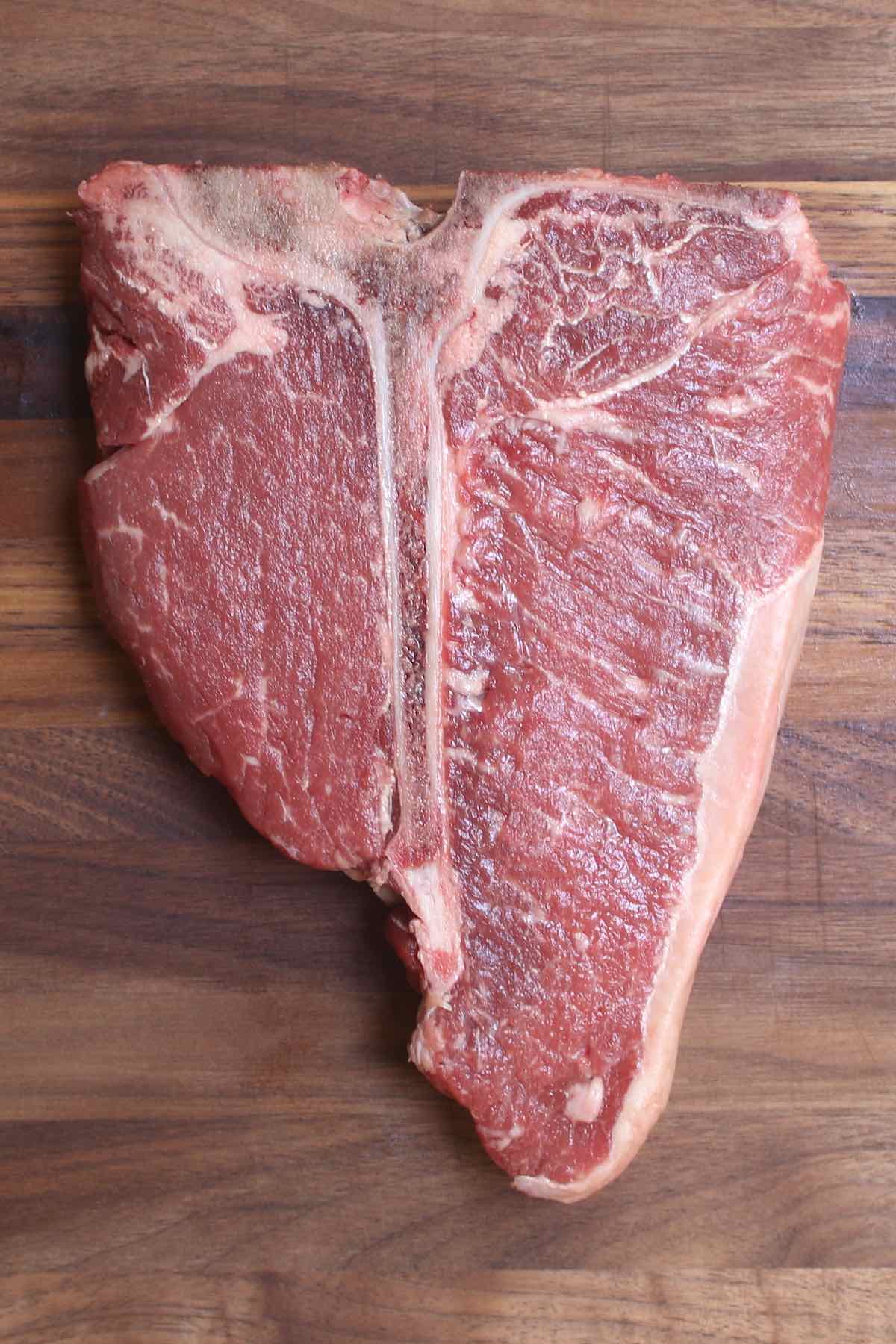 Overhead view of a raw porterhouse steak showing the t-shaped bone in the middle with the striploin on the right side and the much smaller tenderloin (filet mignon) on the left.
