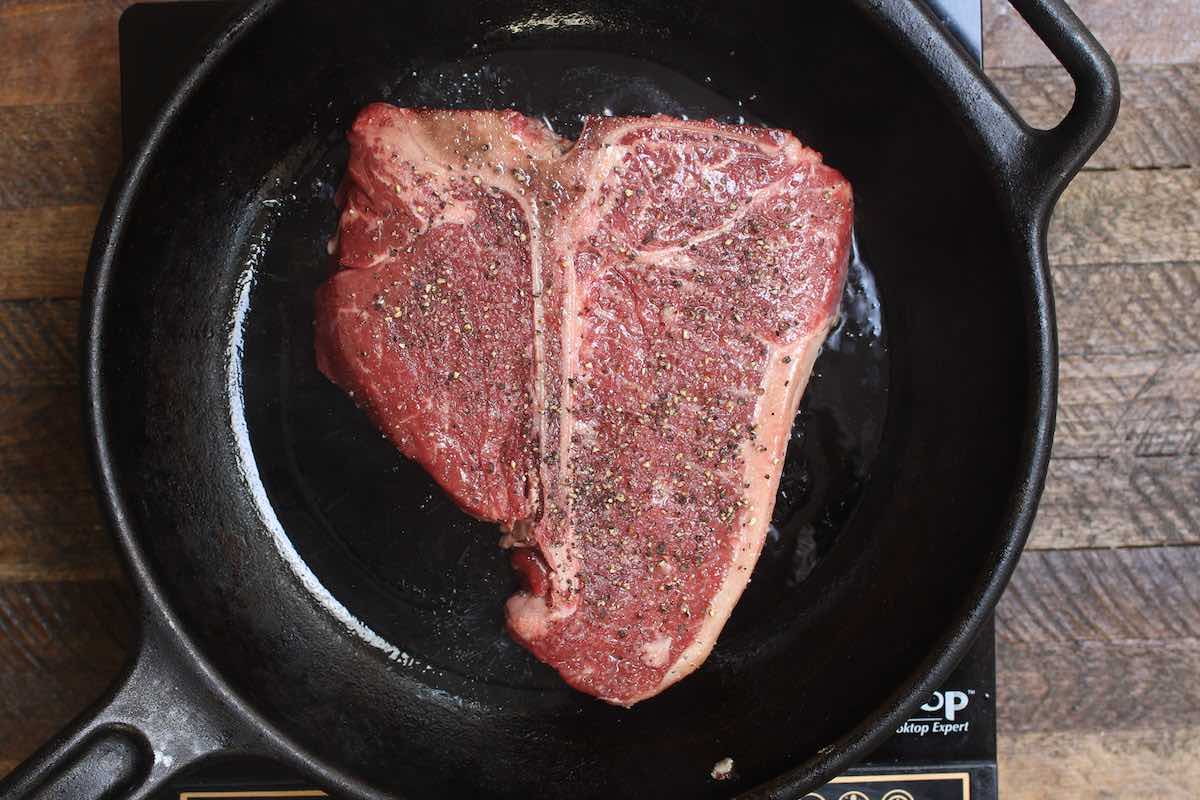 Searing the first side of the steak in a cast-iron skillet.