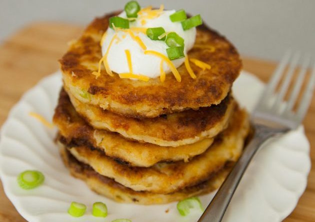 A stack of Mashed Potato Pancakes garnished with sour cream and green onions