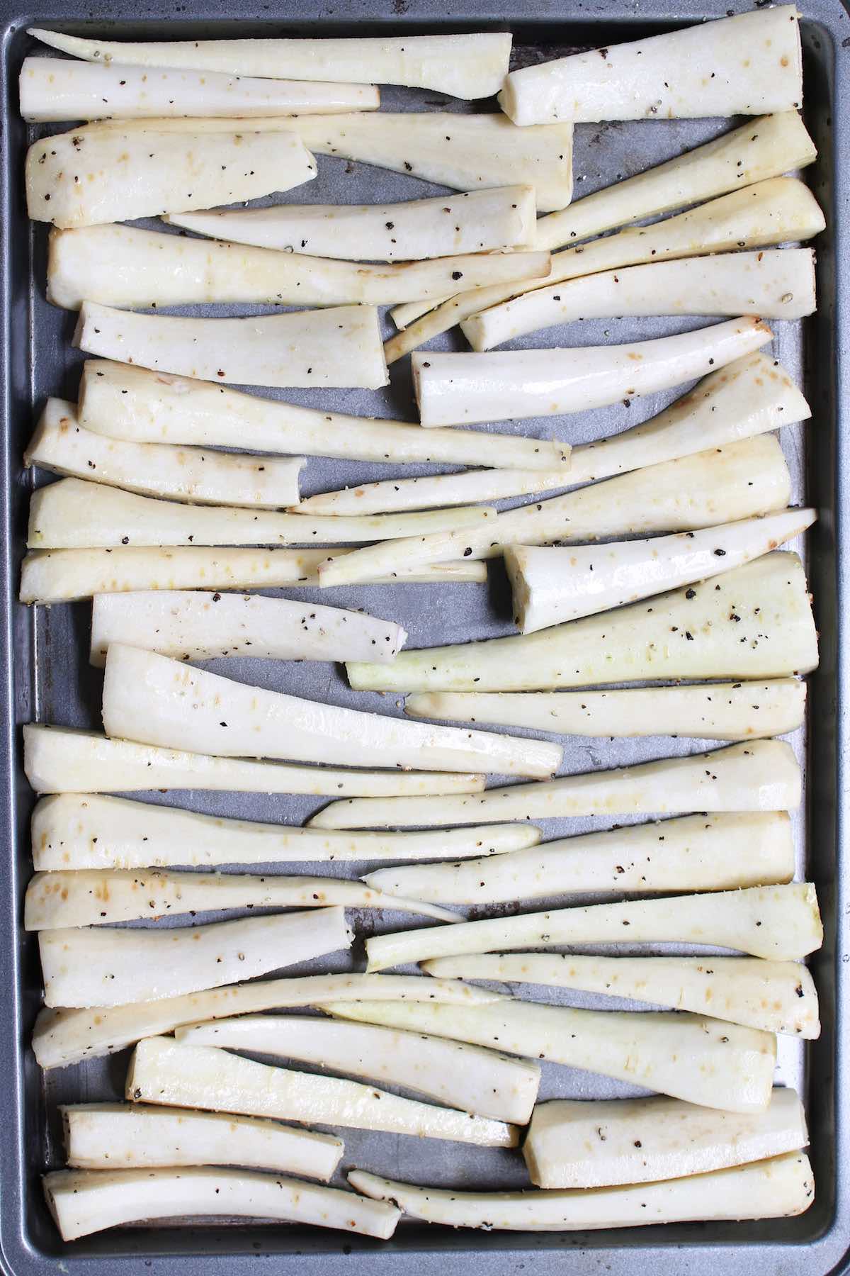 Seasoned parsnips evenly distributed in a single layer on a sheet pan