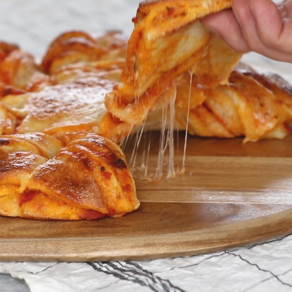 This closeup photo shows an epic cheese pull on a pizza braid during serving