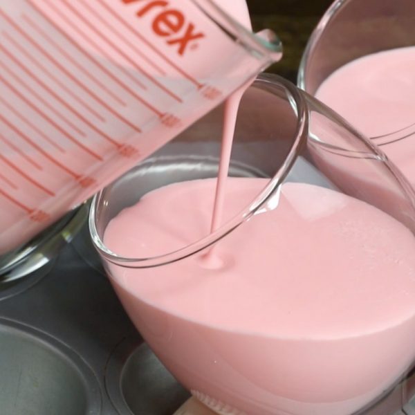 Raspberry Chocolate Mousse - this is a close-up photo of pouring raspberry mousse mixture into a stemless wine glass held on an incline using a muffin tin