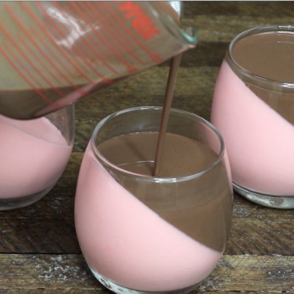 Raspberry Chocolate Mousse - this is a close-up photo of pouring chocolate mousse mixture on top of a raspberry mousse layer in a stemless wine glass