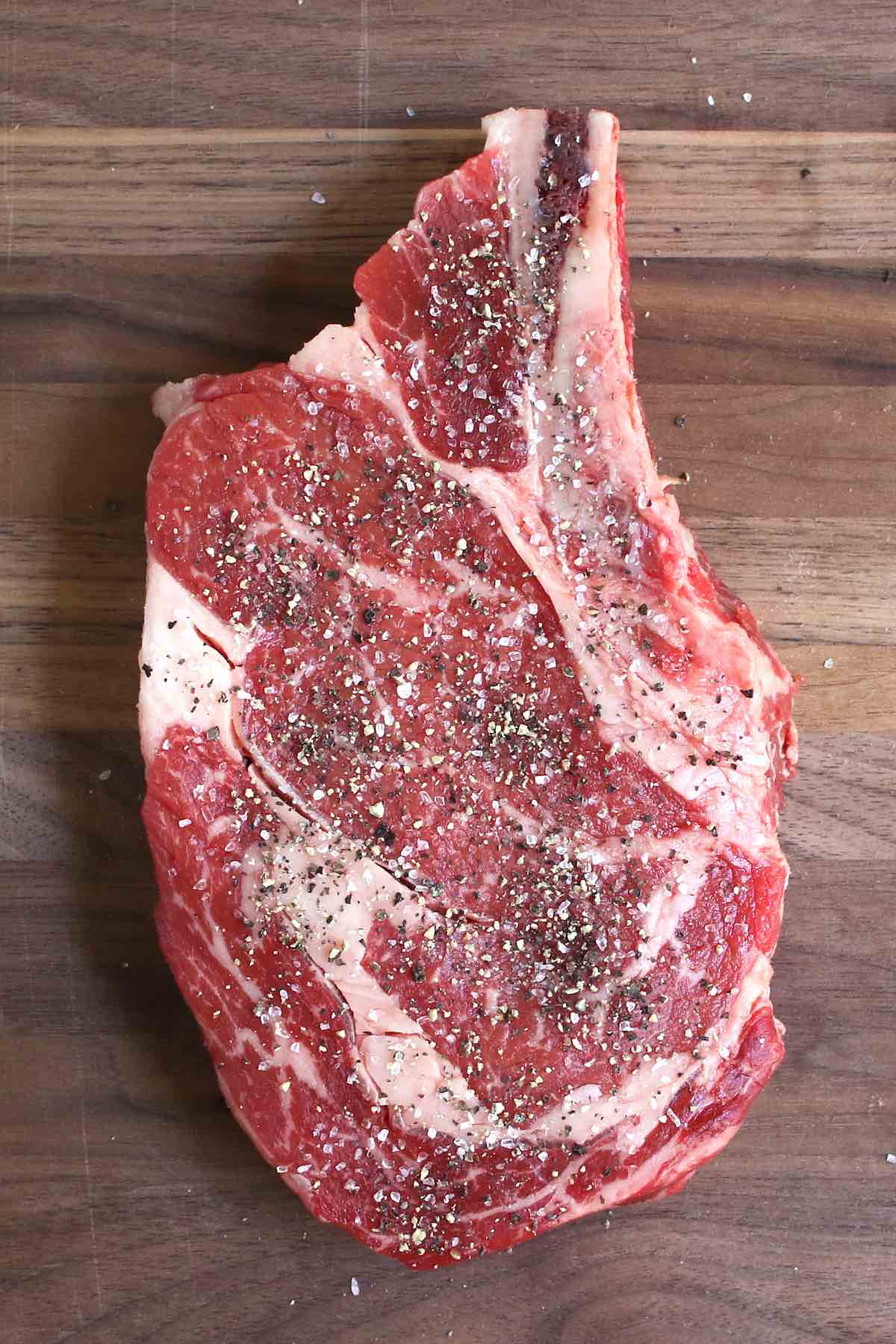Thick cut ribeye seasoned with coarse salt and black pepper, ready for cooking