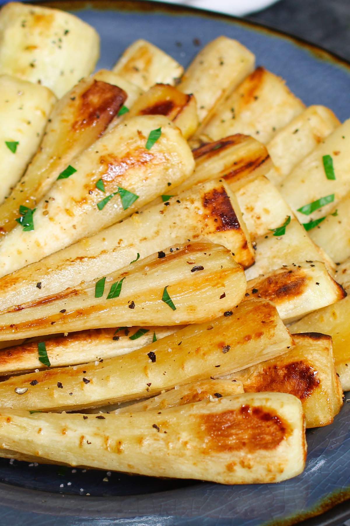 Roasted parsnips served on plate, and topped with chopped parsley.