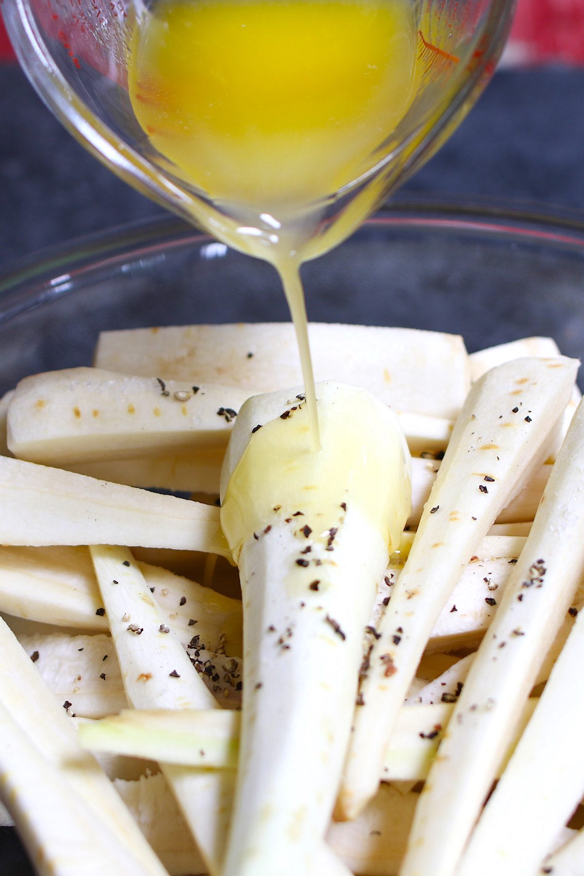 Season parsnips with salt, pepper and melted butter in a clear mixing bowl