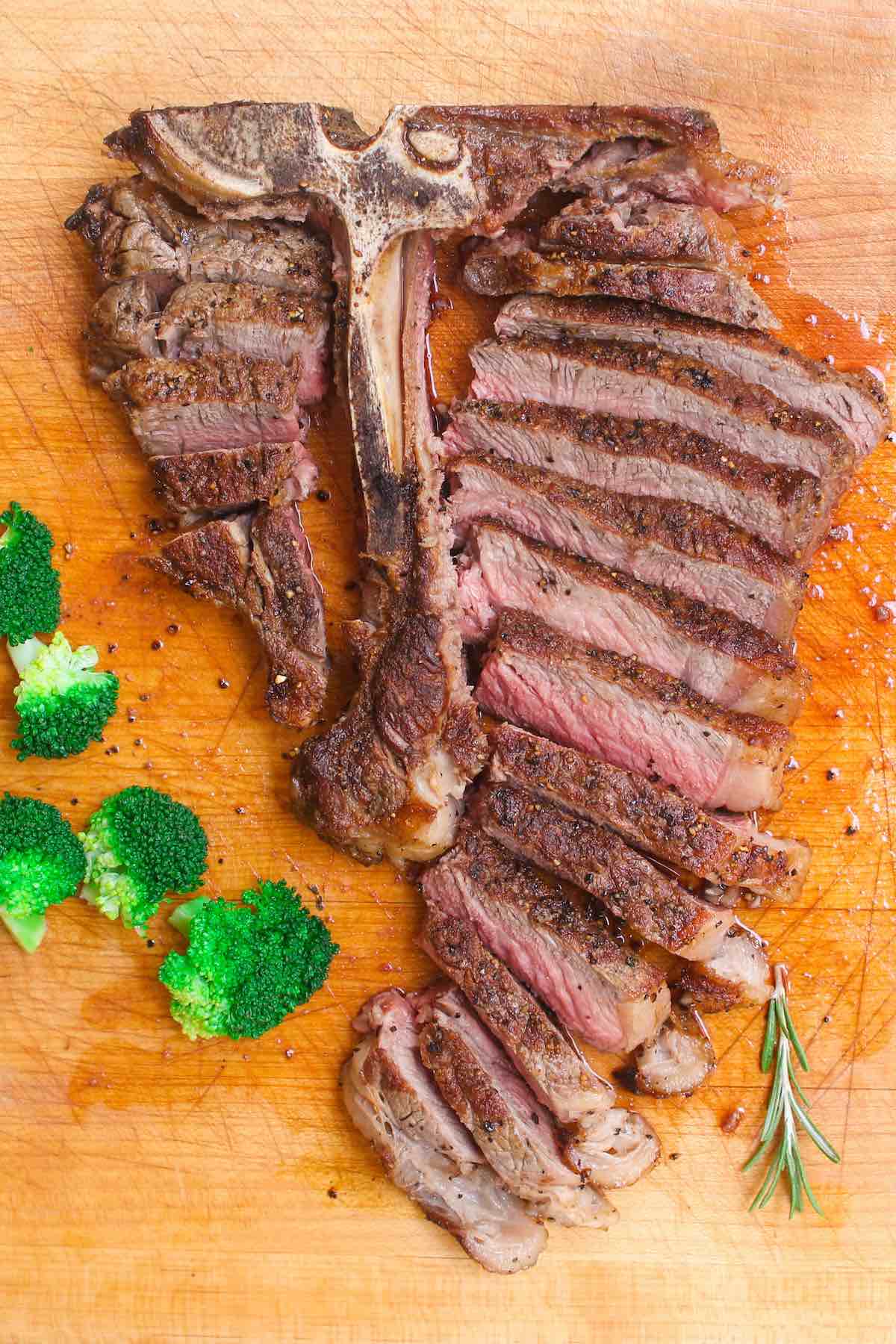 T-bone steak on a cutting board after being prepared for serving by cutting the meat away from the bone and slicing into thin pieces