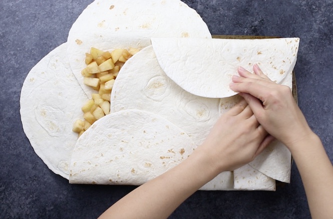 Folding tortillas over the baking sheet to cover the apple filling