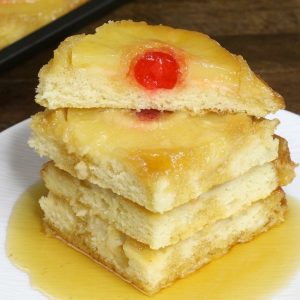 Stack of pineapple upside down pancakes on a serving plate with maple syrup drizzled on top