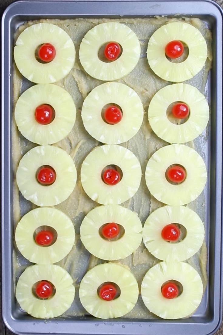 Pineapple rings and maraschino cherries on a baking sheet with brown sugar and butter glaze