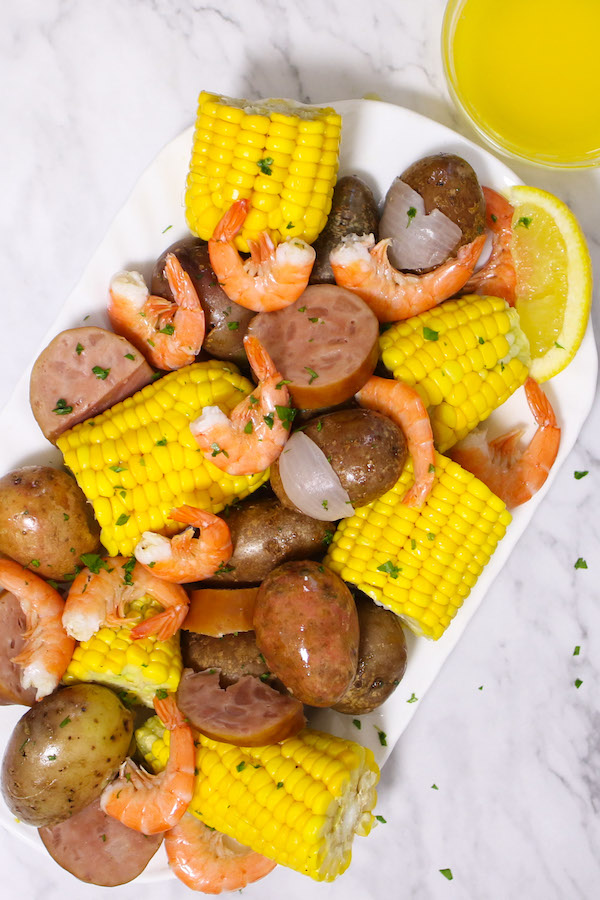 Mouthwatering shrimp boil served on a platter garnished with fresh parsley and with melted butter for dipping on the side. A true southern feast waiting to be eaten!