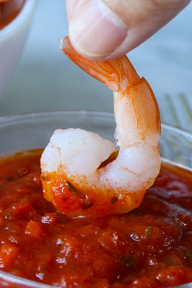 A large peeled shrimp that's been boiled and chilled being dipped in cocktail sauce