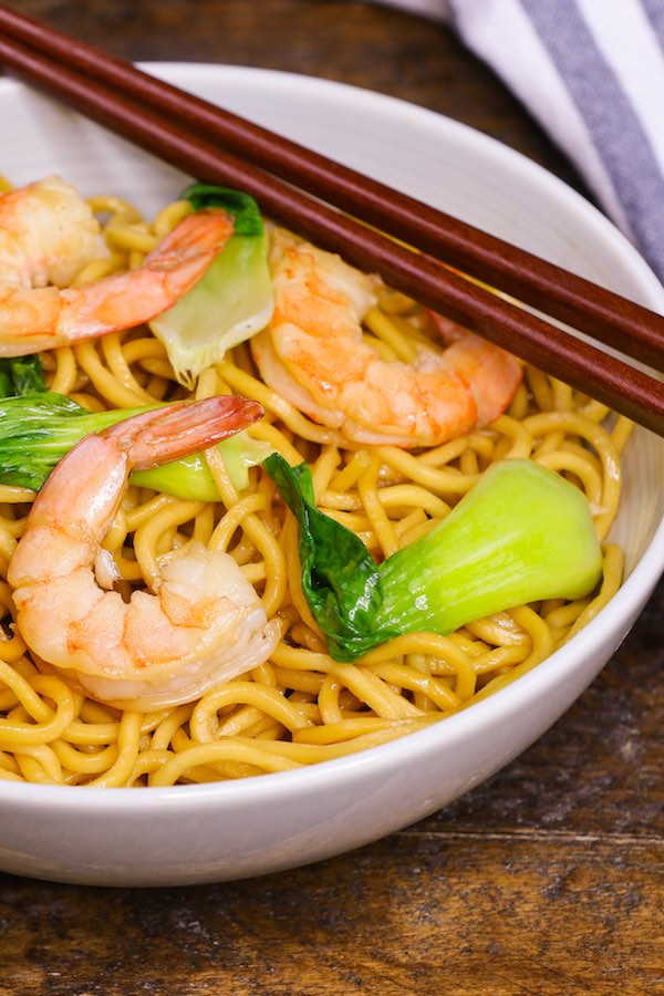 A bowl of chow mein noodles containing shrimp and bok choy, with chopsticks on the side