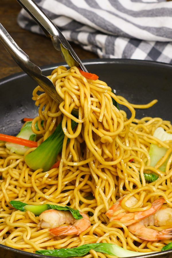 Kitchen tongs picking up fried shrimp noodles out of a frying pan