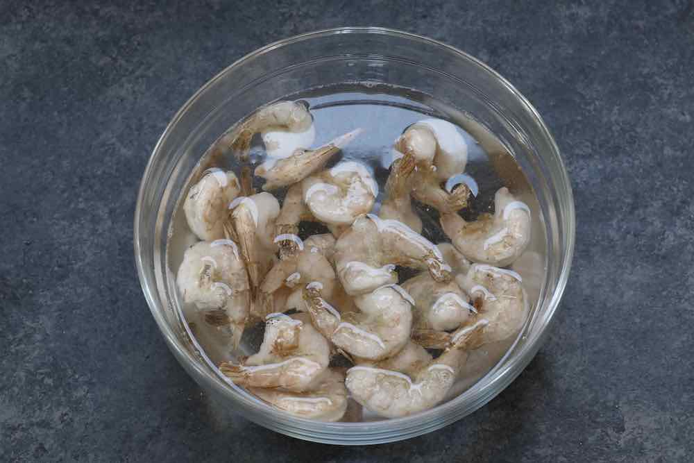 Frozen shrimp thawing in a bowl of cold water