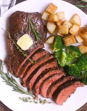 Overhead view of a sirloin steak dinner consisting of sliced top sirloin garnished with fresh rosemary, thyme and a pat of butter, served with sautéed potatoes and broccoli