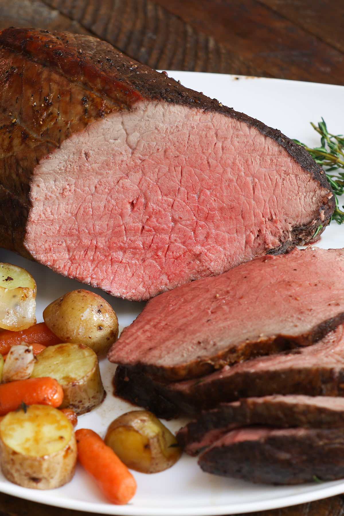 Slices of sirloin tip roast on a serving plate with roasted potatoes and carrots