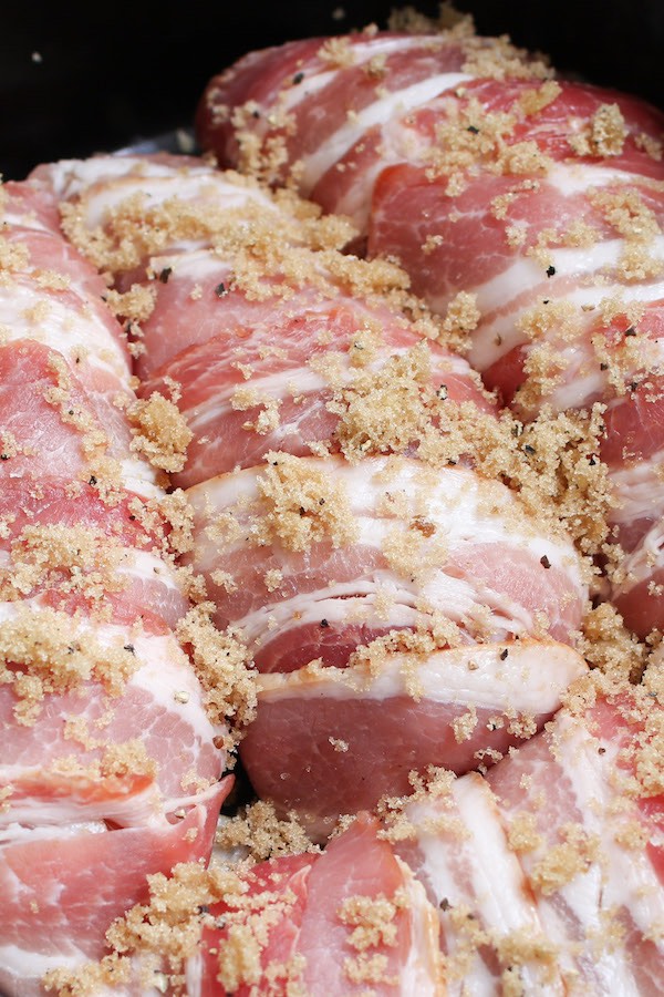 Bacon wrapped chicken breasts in the crock pot with brown sugar, salt and pepper sprinkled on top ready for slow cooking.
