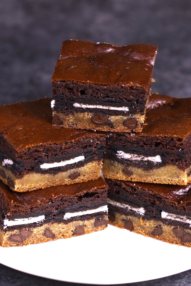 A stack of Slutty Brownies on a serving platter showing the 3 layers of cookie dough, Oreo cookies and brownies