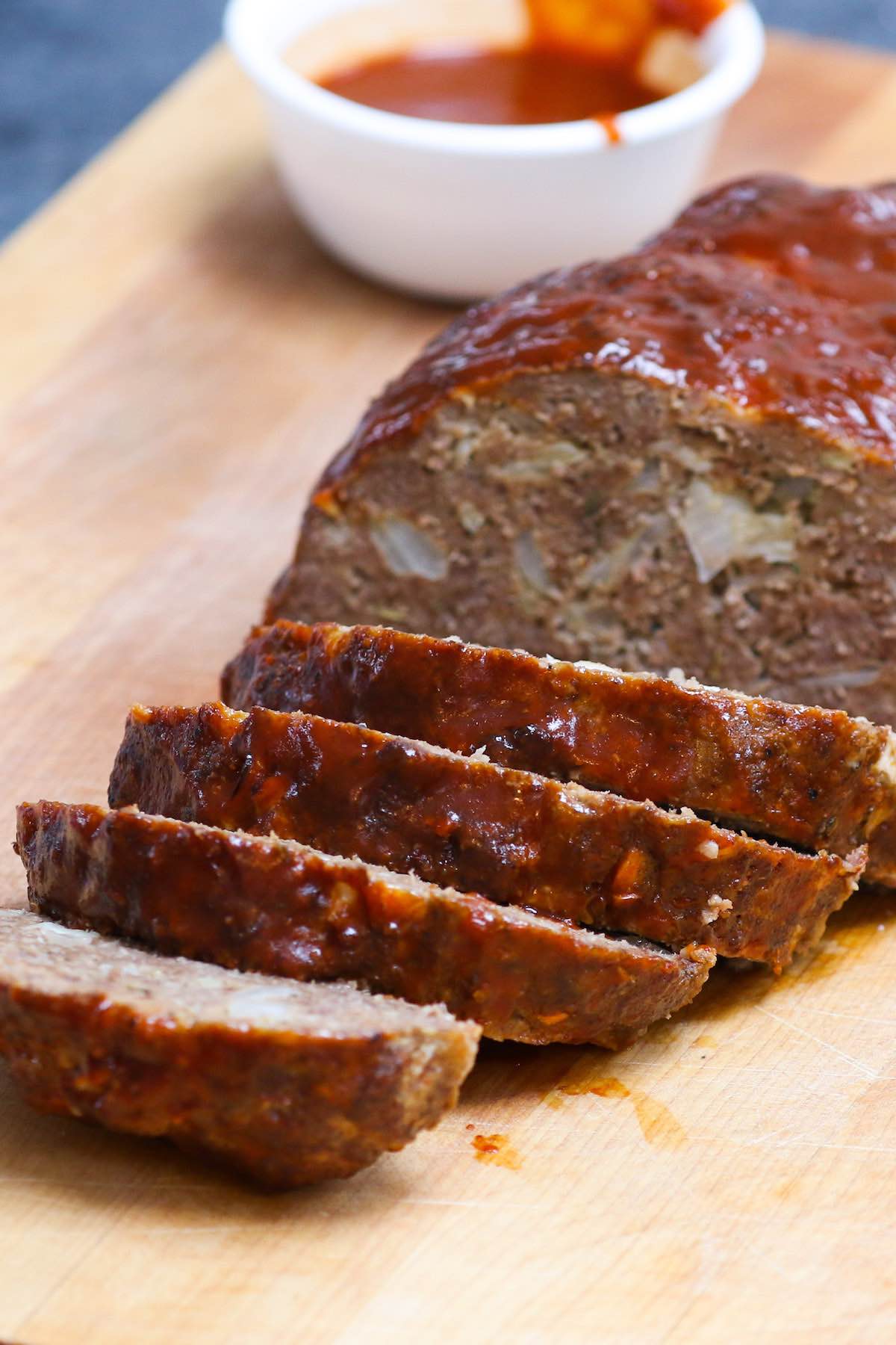 Sliced meatloaf fresh out of the smoker with BBQ sauce on the side