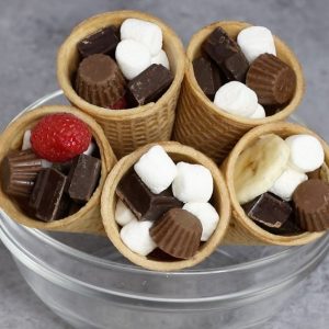 Easy S’mores Campfire Cones – An easy and fun summer treats recipe. All you need is only a few ingredients: ice cream cones, mini-marshmallows, banana, raspberry, mini peanut butter cups and chocolate bars. This recipe can be customized with your favorite candies or fruits. Campfire recipe. Quick and easy recipe. Video recipe. | Tipbuzz.com