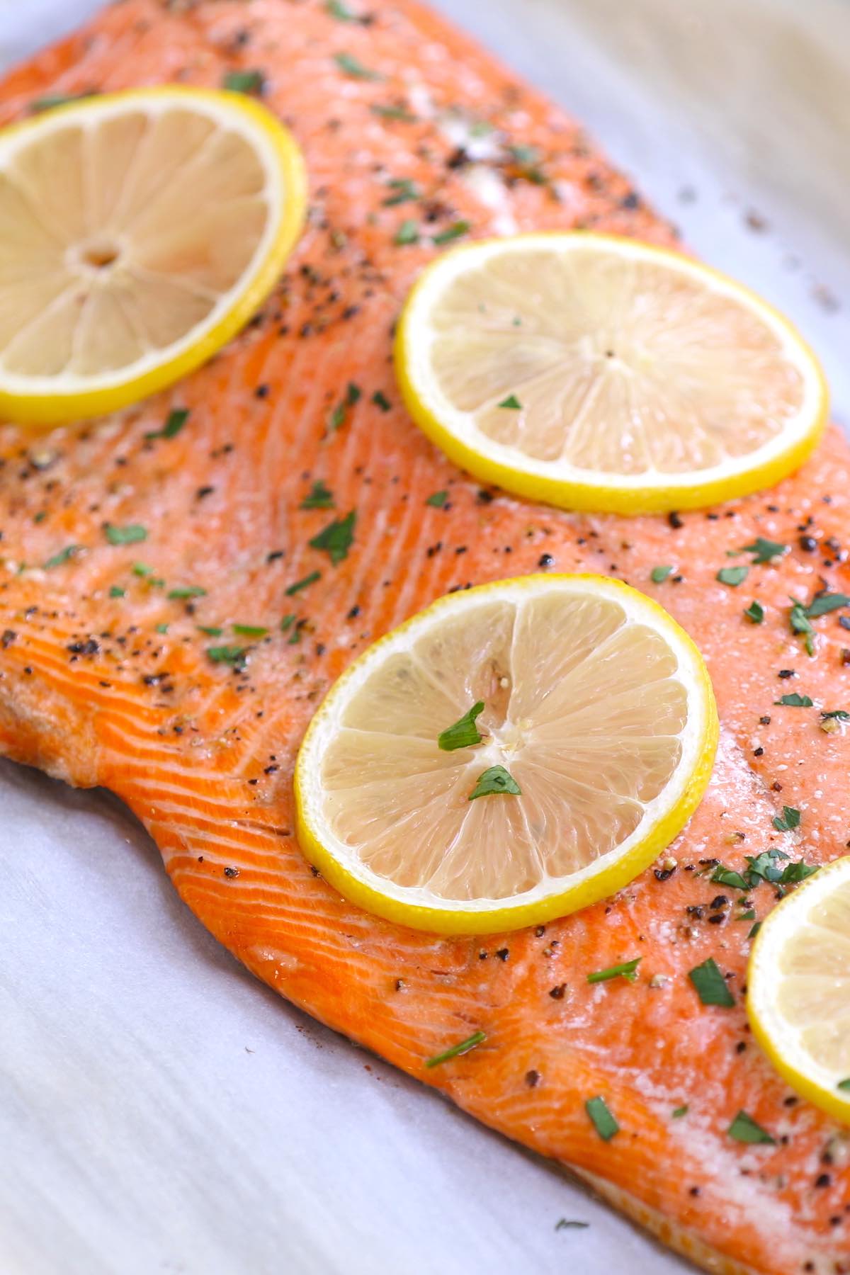 A fillet of baked sockeye salmon with lemon slices and fresh herbs