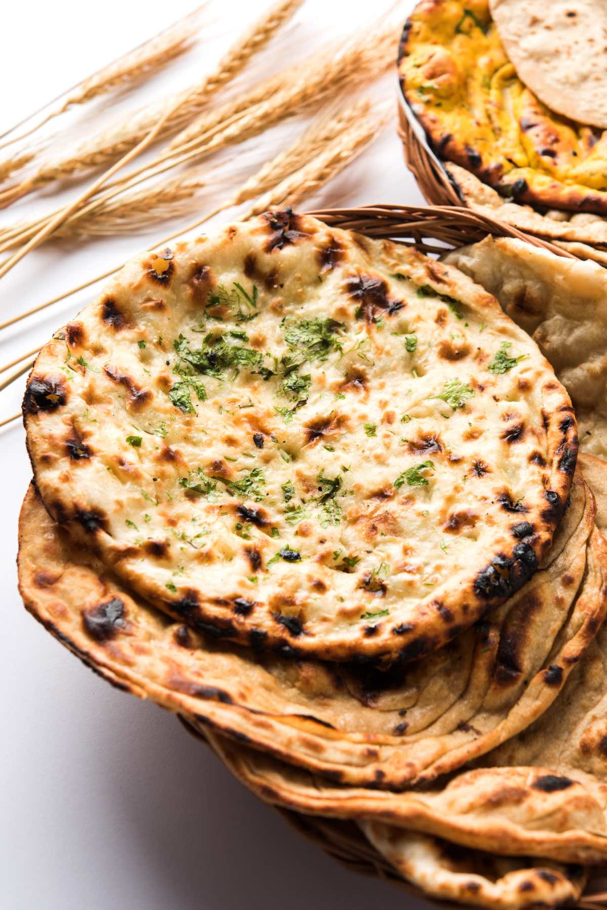 A stack of fresh sourdough naan with crispy edges and fresh cilantro for garnish