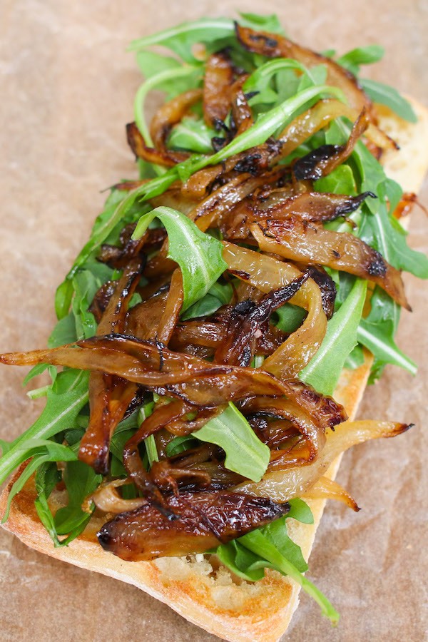 Assembling the steak sandwich – Top the bottom half of bread with arugula and caramelized onions.