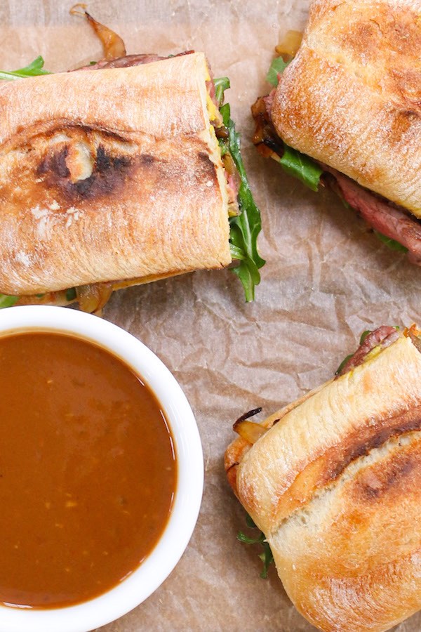 Assembled steak sandwiches cut in half and serving on a cutting board with dressing