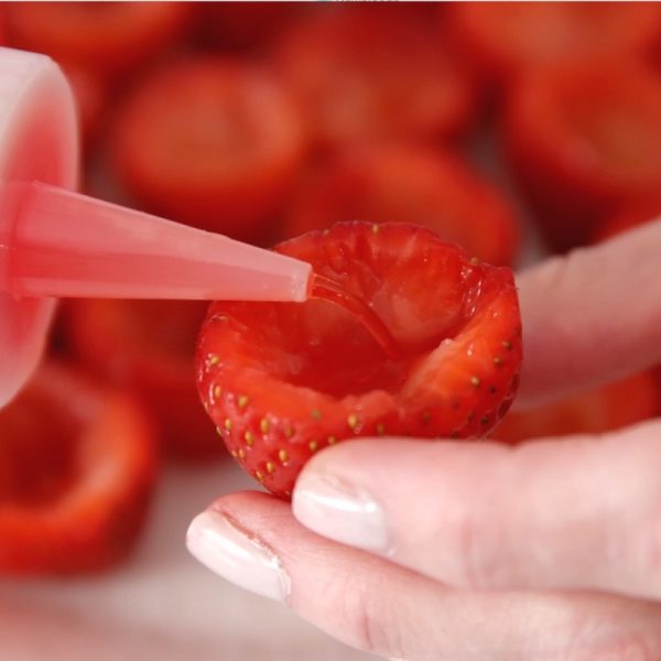 Adding strawberry jello to a hulled strawberry using a squeeze bottle when making Strawberry Jello Shots
