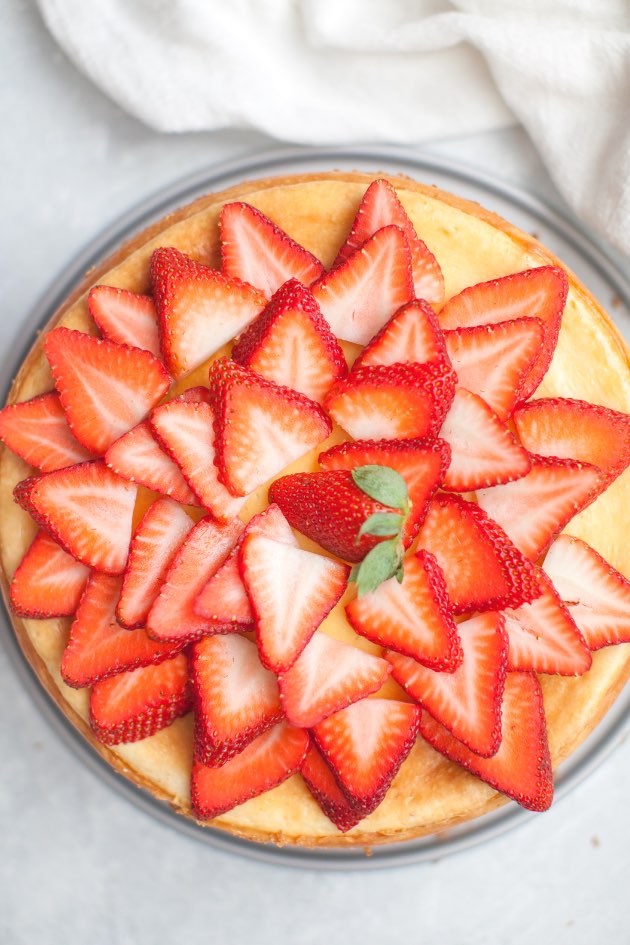 Overhead view of a baked strawberry white chocolate cheesecake with fresh sliced strawberries on top