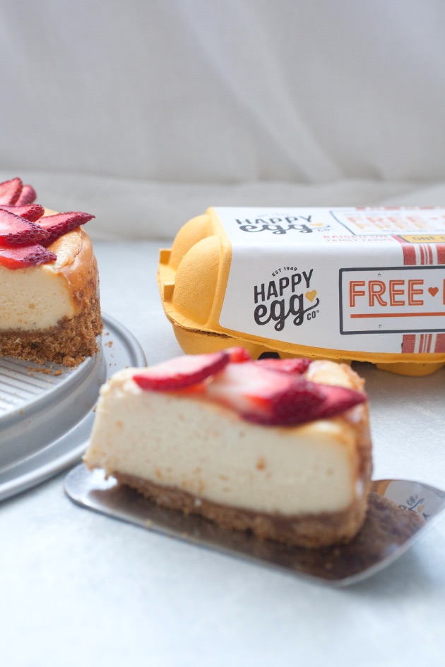 A slice of strawberry white chocolate cheesecake showing Happy Egg free range eggs in the background