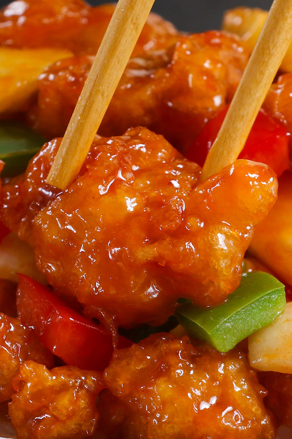 A closeup of sweet and sour chicken with bell peppers, onions and pineapple all coated a sticky sauce