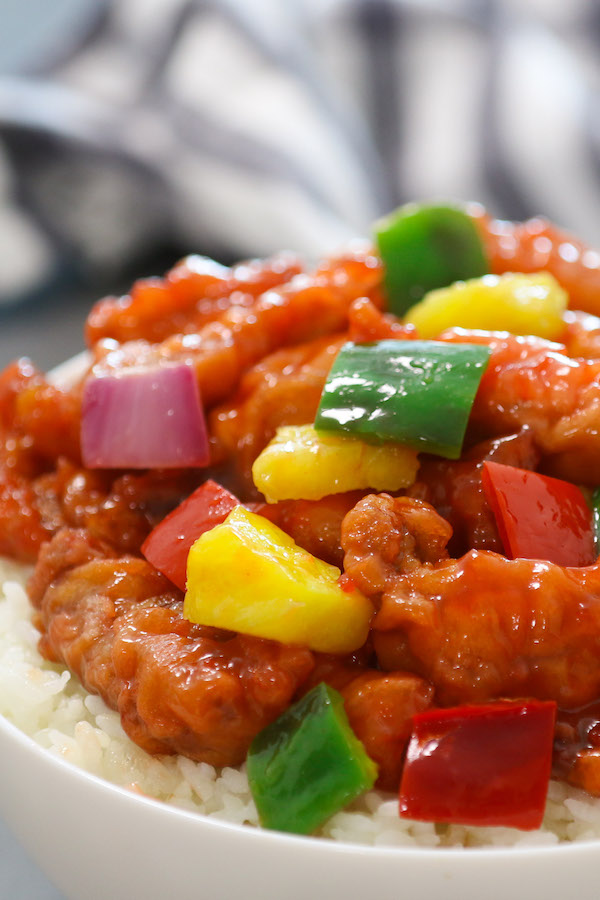 Closeup view of sweet and sour pork with purple onions, red and green bell peppers, pineapple on a bed of steamed rice