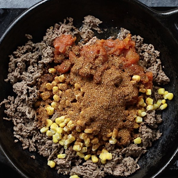 Taco Casserole - this photo shows browned beef in a cast iron skillet with salsa, corn and taco seasoning being added in to make this recipe.