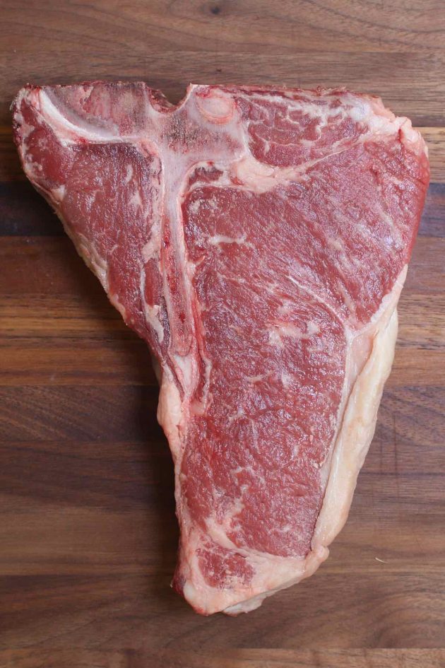 Overhead view of a raw tbone steak showing the t-shaped bone in the middle with the striploin on the right side and the much smaller tenderloin (filet mignon) on the left