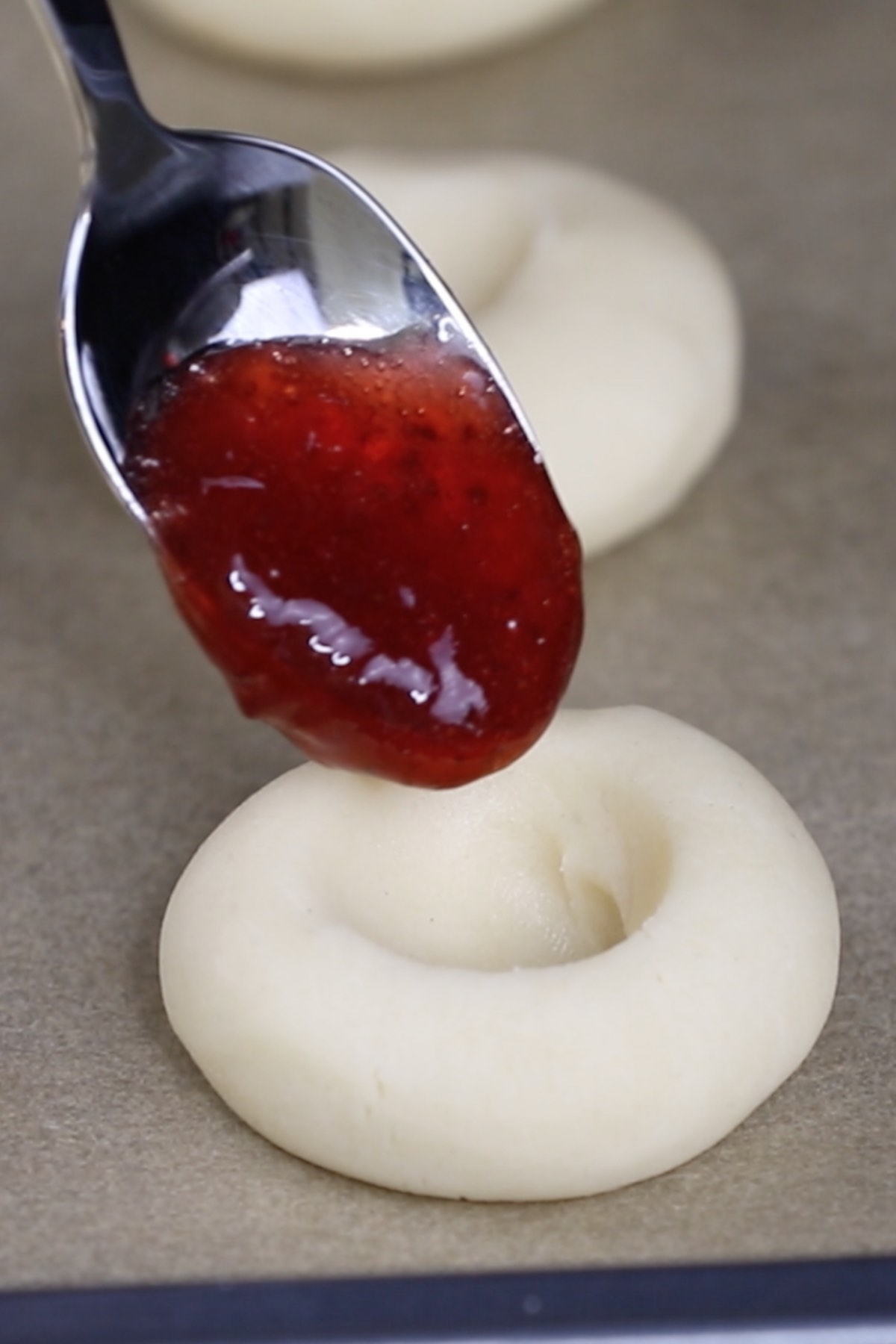 Closeup of spooning jam into an indented cookie dough ball.