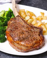 Tomahawk steak on a serving plate with potatoes and broccoli