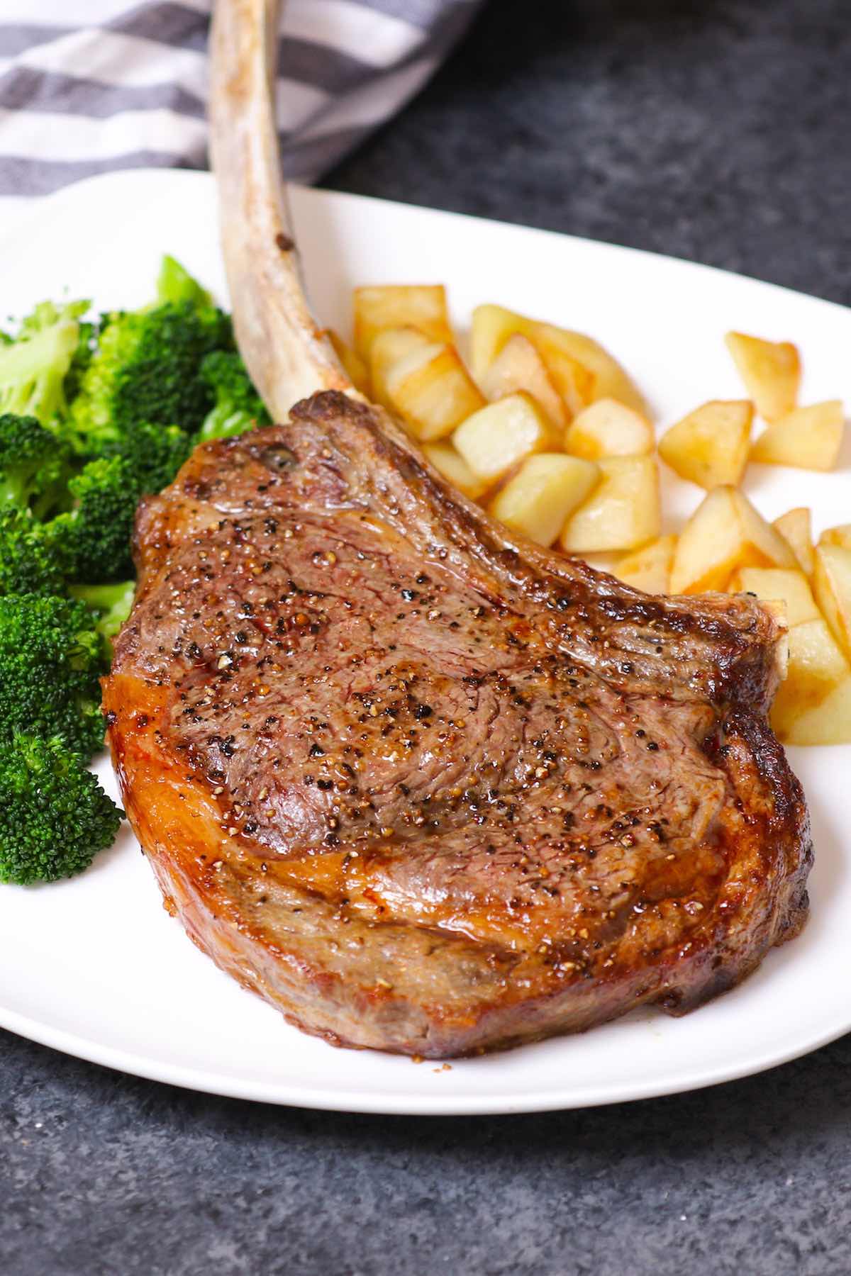 Tomahawk steak on a serving plate with potatoes and broccoli