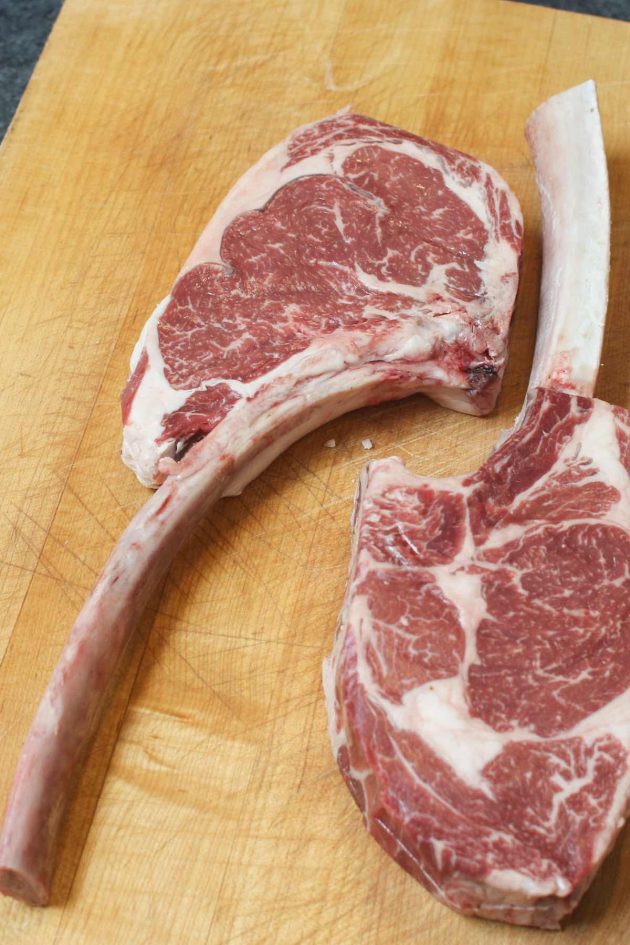 Raw tomahawk steaks showing the marbling of the meat and the long bone